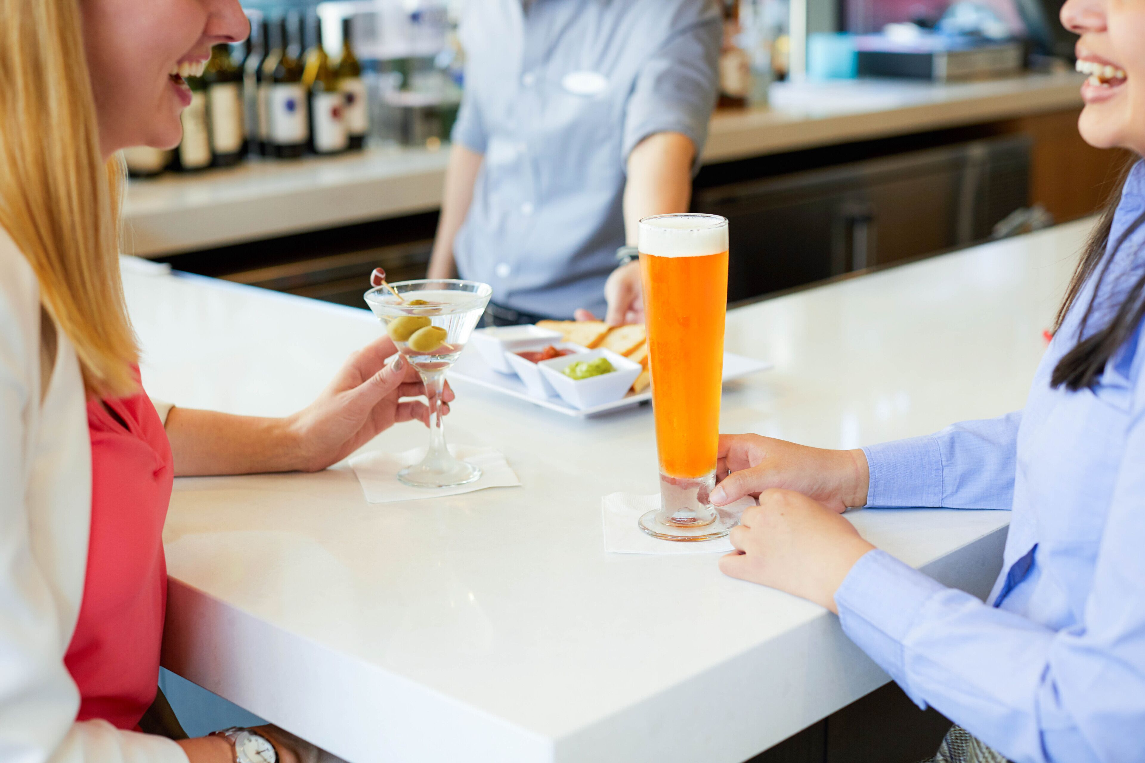 Un bar avec un grand verre de bière, un verre à martini garni d’olives et une assiette de collations.