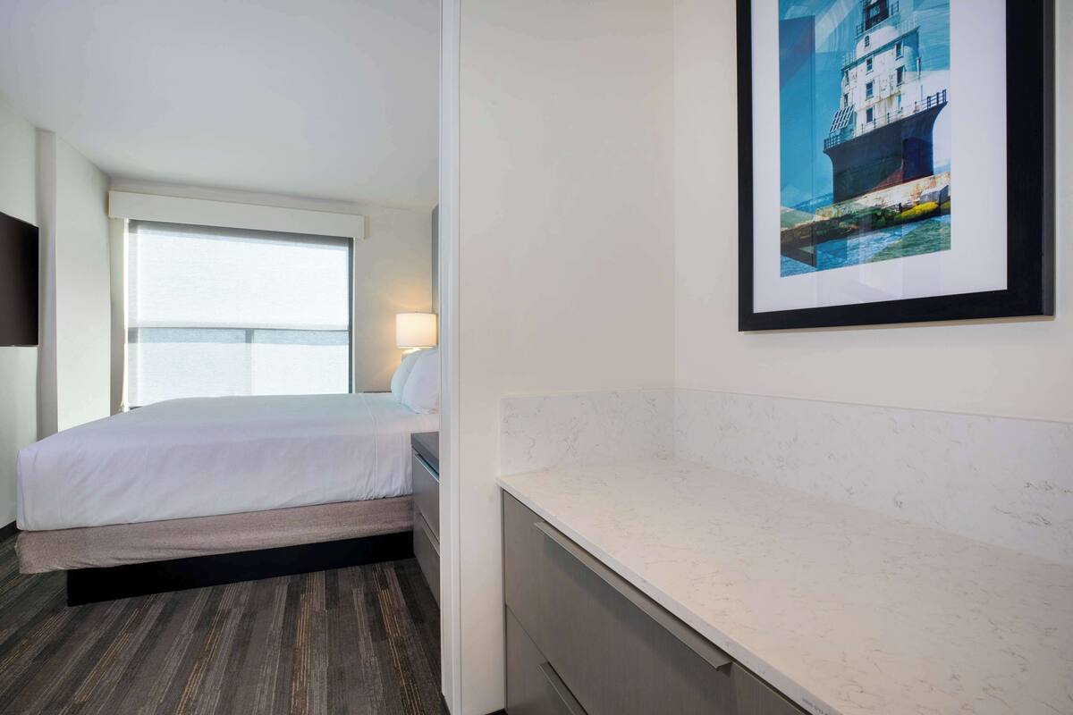 A hotel room with a bed, a bedside lamp, a framed picture on the wall, and a marble countertop.