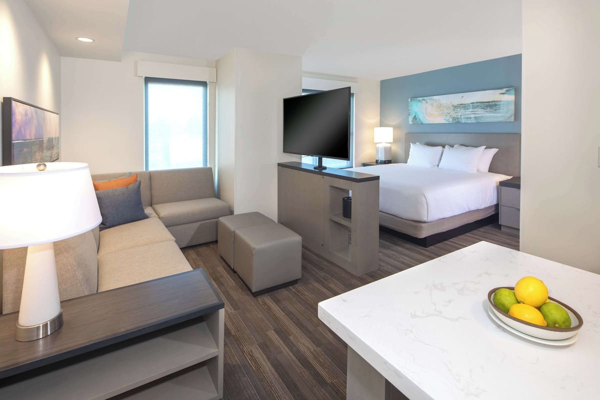 A hotel room with a sofa, a bed, a TV, a desk, and a fruit bowl.