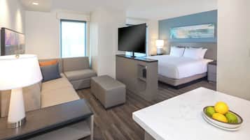 Une chambre d’hôtel équipée d’un canapé, d’un lit, d’une télévision, d’un bureau et d’un panier de fruits.