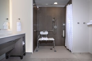 Une salle de bain moderne équipée d’une douche, de toilettes avec une barre d’appui et d’un meuble-lavabo avec un miroir et un porte-serviettes.