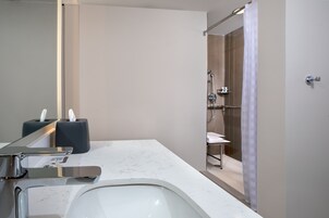 A modern bathroom with a white sink, a mirror, a towel rack, and a shower area with a glass door.