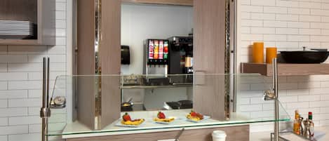 A modern kitchen with a glass display case containing breakfast items, a coffee machine, and a condiment station.