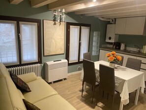 A modern kitchen with white cabinets, a dining table with four chairs, and a radiator below a window.