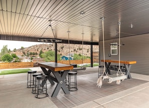 An outdoor patio with a wooden table and bar stools, a hanging swing, and a view of a hilly landscape. - BLACK SHEEP INN Newly Constructed Merino #1 of 4 Units (Cedar City)
