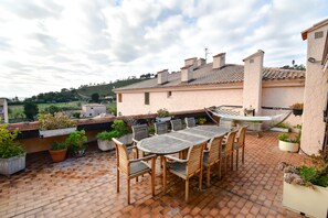 Una terrazza sul tetto con un tavolo rotondo e sedie, circondata da piante in vaso e vista sulla campagna.