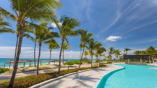 A resort pool area with palm trees, a beach view, and a covered seating area. - Breathless 4You, Oceanfront Penthouse (Cap Cana)