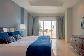 A hotel room with a large bed, a dresser, a lamp, and a view of the outdoors through a sliding glass door. - Breathless 4You, Oceanfront Penthouse (Cap Cana)