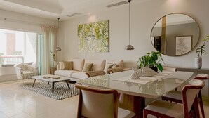 A modern living room with a glass dining table, beige sofas, and a large abstract painting. - Breathless 4You, Oceanfront Penthouse (Cap Cana)
