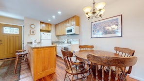 A kitchen with wooden cabinets, a dining table with chairs, a refrigerator, a microwave, and a chandelier.