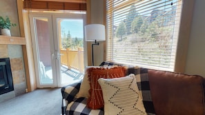 Un salon chaleureux avec un canapé à carreaux, une cheminée et une vue sur une terrasse en bois et des arbres.