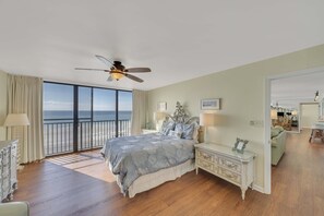 A bedroom with a large bed, a ceiling fan, and a view of the ocean through a sliding door.