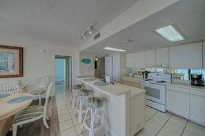 A modern kitchen with white cabinets, a central island with stools, and a dining area with a table and chairs.