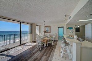 A dining area with a view of the ocean, a kitchen with a bar, and a balcony with a railing.