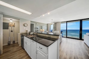 A modern kitchen with a large island, a dining area with a view, and a spacious living room with a balcony overlooking the ocean.