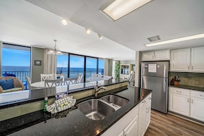 A modern kitchen with a large island, stainless steel appliances, and a view of the ocean.