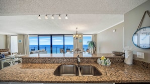 A kitchen with granite countertops, a double sink, and a view of the ocean through large windows. - FREE Beach Service for 2, FREE Daily Golf & Perks! Beachfront Seachase E802 (Panama City Beach)