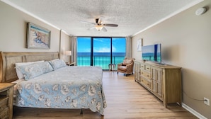 A bedroom with a large bed, a ceiling fan, a TV, a dresser, and a view of the ocean. - FREE Beach Service for 2, FREE Daily Golf & Perks! Beachfront Seachase E802 (Panama City Beach)