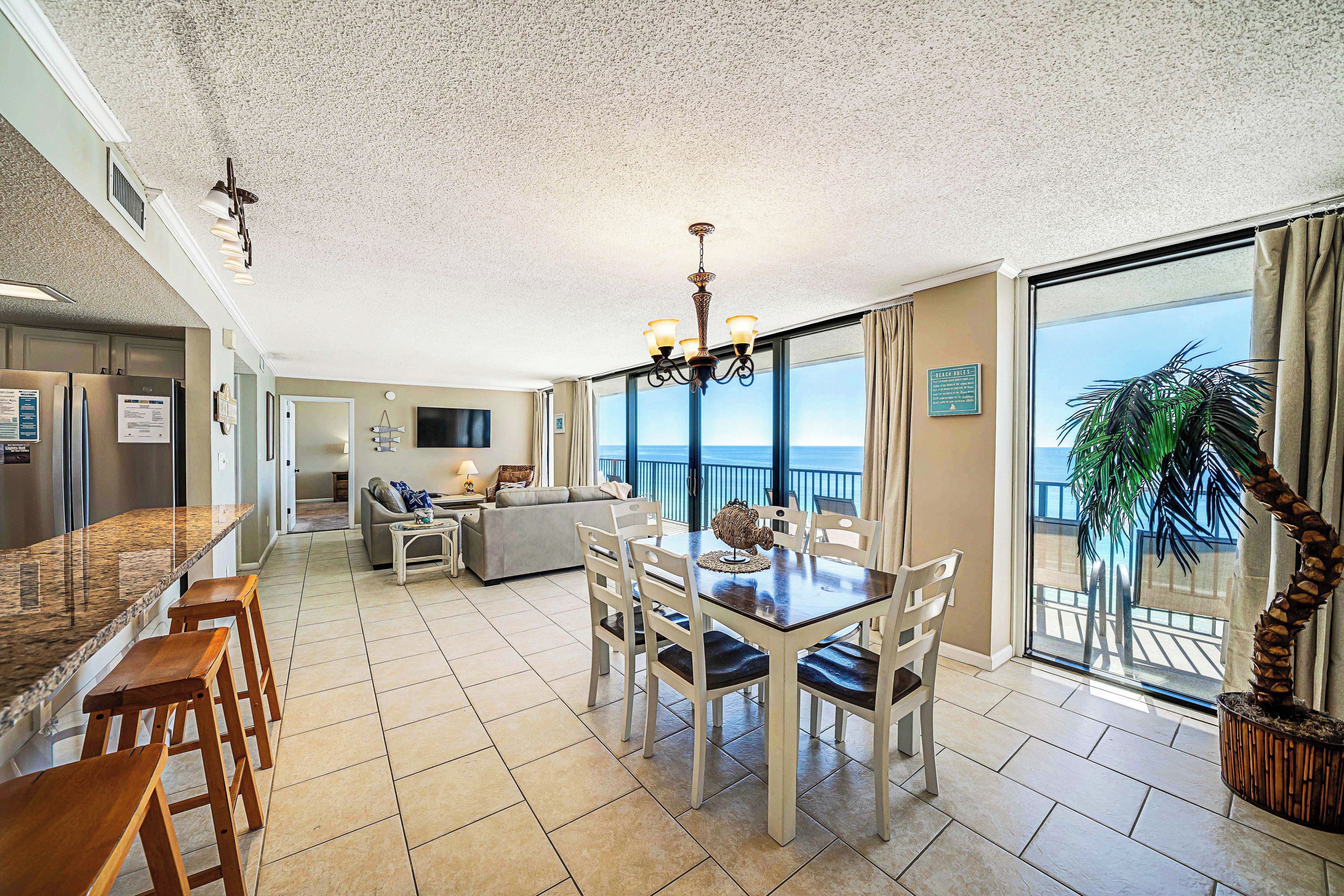 A spacious living area with a dining table, chairs, and a large window offering a view of the ocean.