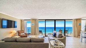 A spacious living room with a large flat-screen TV, comfortable seating, and a balcony with a view of the ocean. - FREE Beach Service for 2, FREE Daily Golf & Perks! Beachfront Seachase E802 (Panama City Beach)