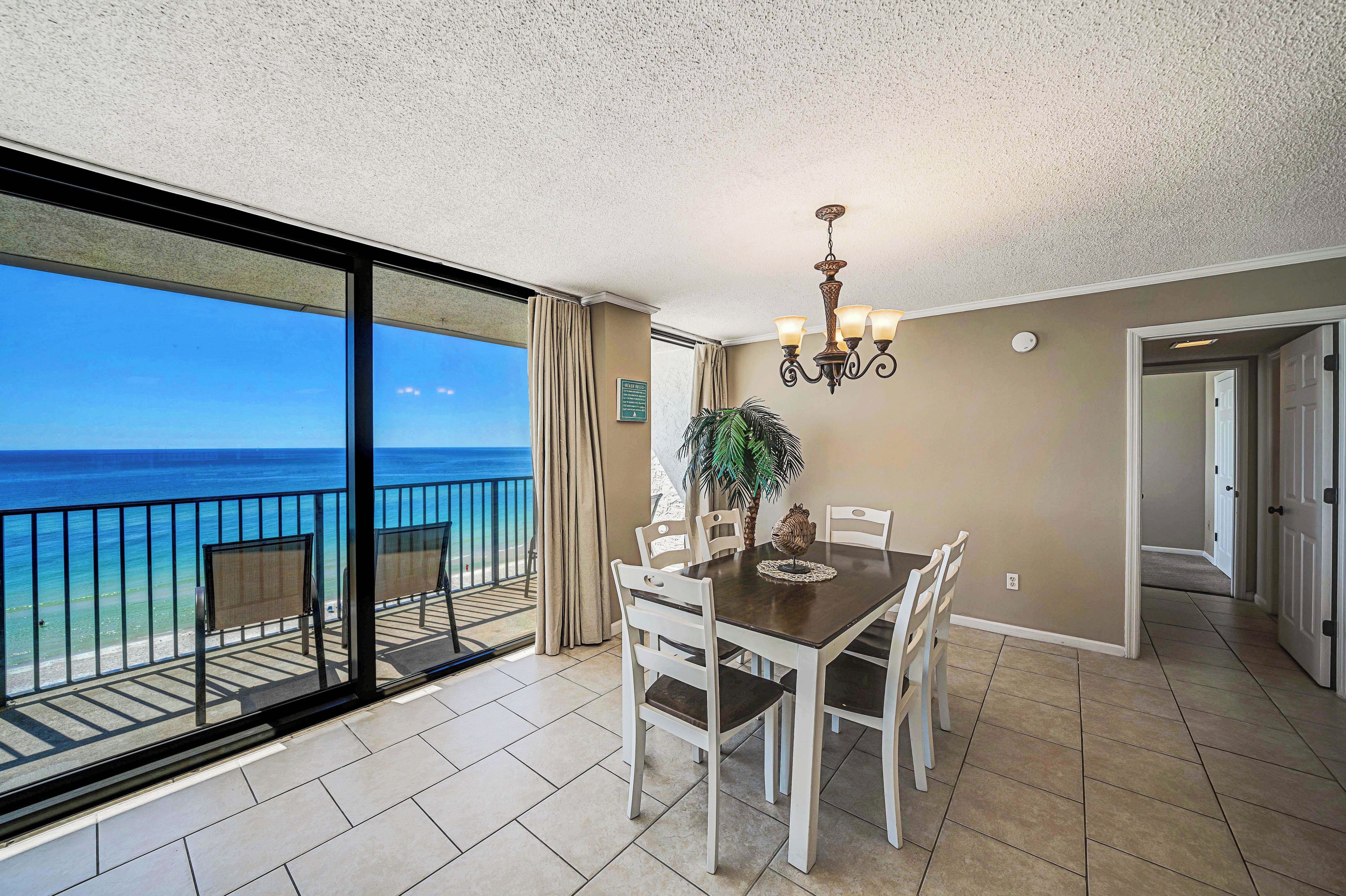 A dining area with a view of the ocean, a chandelier, and a potted plant.