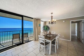 A dining area with a view of the ocean, a chandelier, and a potted plant.