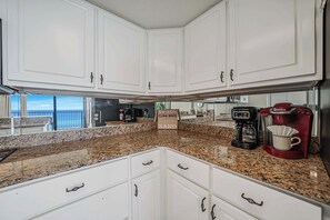 A kitchen with white cabinets, a granite countertop, a coffee maker, and a sign that reads "beach clam bake sand".