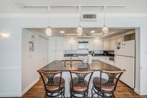 Una cocina con isla central, taburetes de bar, microondas, estufa y refrigerador.