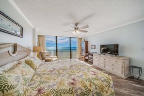 Un dormitorio con una cama grande, televisión, ventilador de techo y vista al océano.