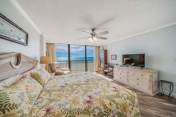 A bedroom with a large bed, a television, a ceiling fan, and a view of the ocean.