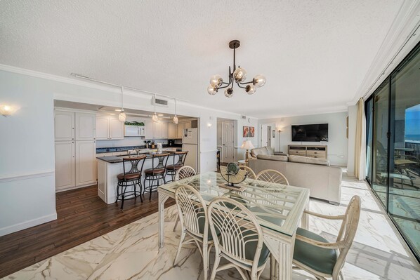A modern kitchen with white cabinetry, a central island, and a dining area with a glass table and wicker chairs.