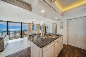 A spacious kitchen with a large island, a dining area with a view of the ocean, and a balcony with a view of the beach.