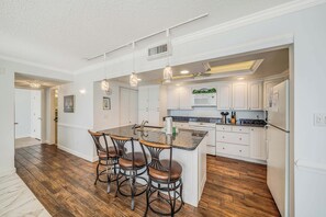 A modern kitchen with a central island, bar stools, and a dining area.