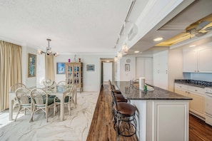 Una cocina moderna con encimera de mármol, taburetes de bar de madera y una zona de comedor con sillas de mimbre.