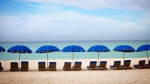 Una playa con hileras de sombrillas azules y sillones de madera.