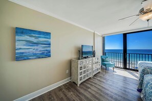 Una habitación con amplia vista al océano, ventilador de techo, televisor sobre un mueble y cama con ropa de cama estampada.