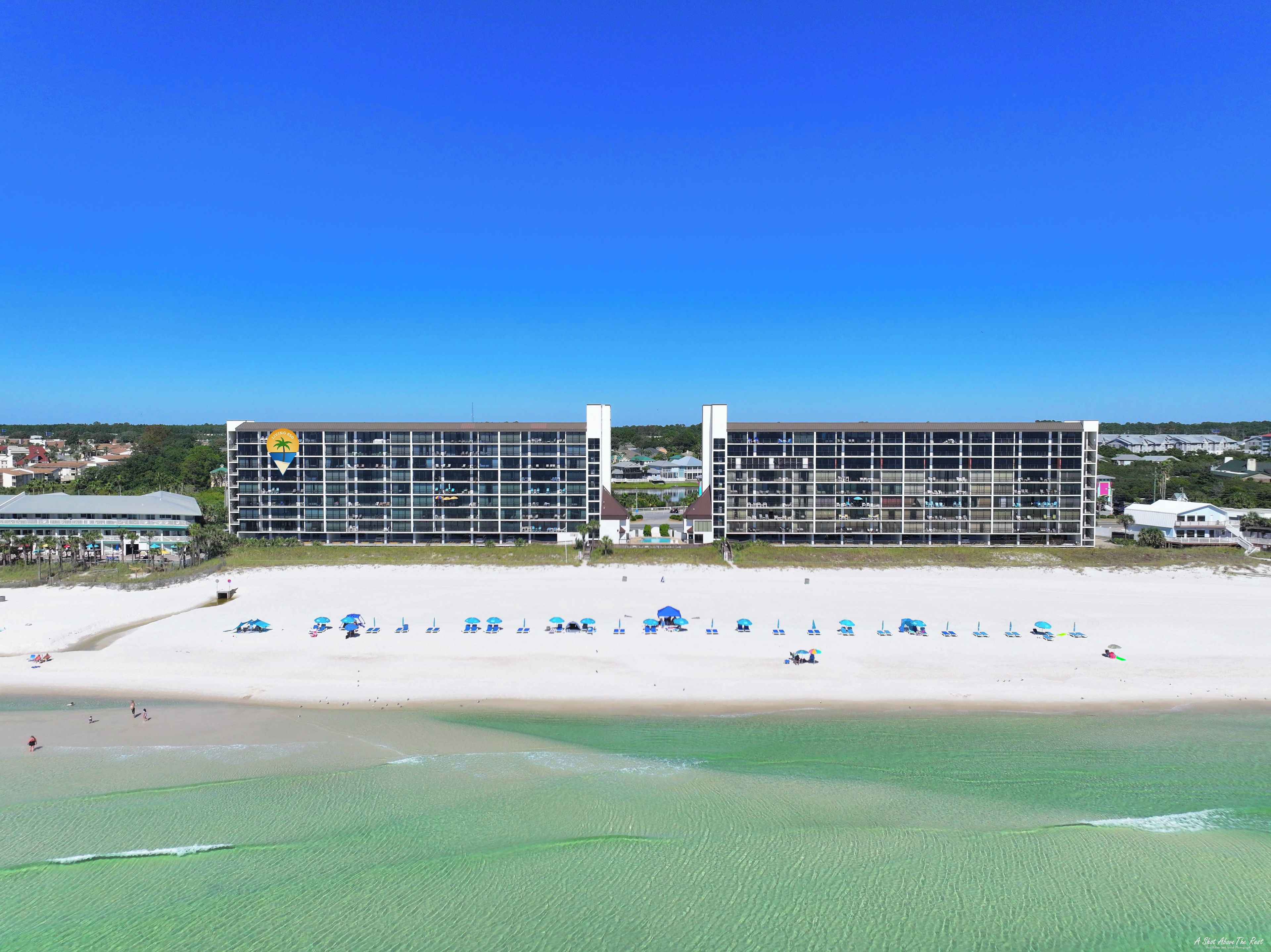 A hotel with multiple floors, a beach in the foreground, and a clear blue sky.