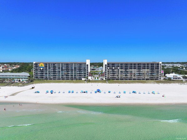 A hotel with multiple floors, a beach in the foreground, and a clear blue sky.