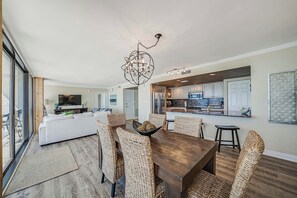 A spacious living room with a dining area, a kitchen in the background, and a large window providing natural light.