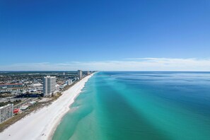 A coastal cityscape with a long beach, clear blue waters, and high-rise buildings along the shore.
