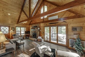 A spacious log cabin interior with a fireplace, multiple seating areas, and large windows.