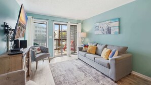 Una sala de estar con un sofá gris, una mesa de centro, un televisor y un escritorio con una computadora.