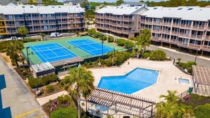 Un hotel de varios pisos con cancha de tenis, piscina y un patio cubierto.