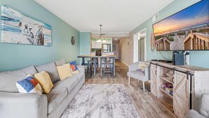 Una sala de estar con sofá, una mesa de centro, televisor y una cocina al fondo.