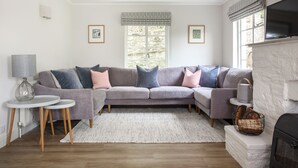 A modern living room with a grey sectional sofa, a white fireplace, and a large window with patterned valance. - 4 BR (Sleeps 7) in Salcombe overlooking beach (Salcombe)