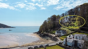 A coastal view with a beach, a road with parked cars, and a house surrounded by greenery. - 4 BR (Sleeps 7) in Salcombe overlooking beach (Salcombe)