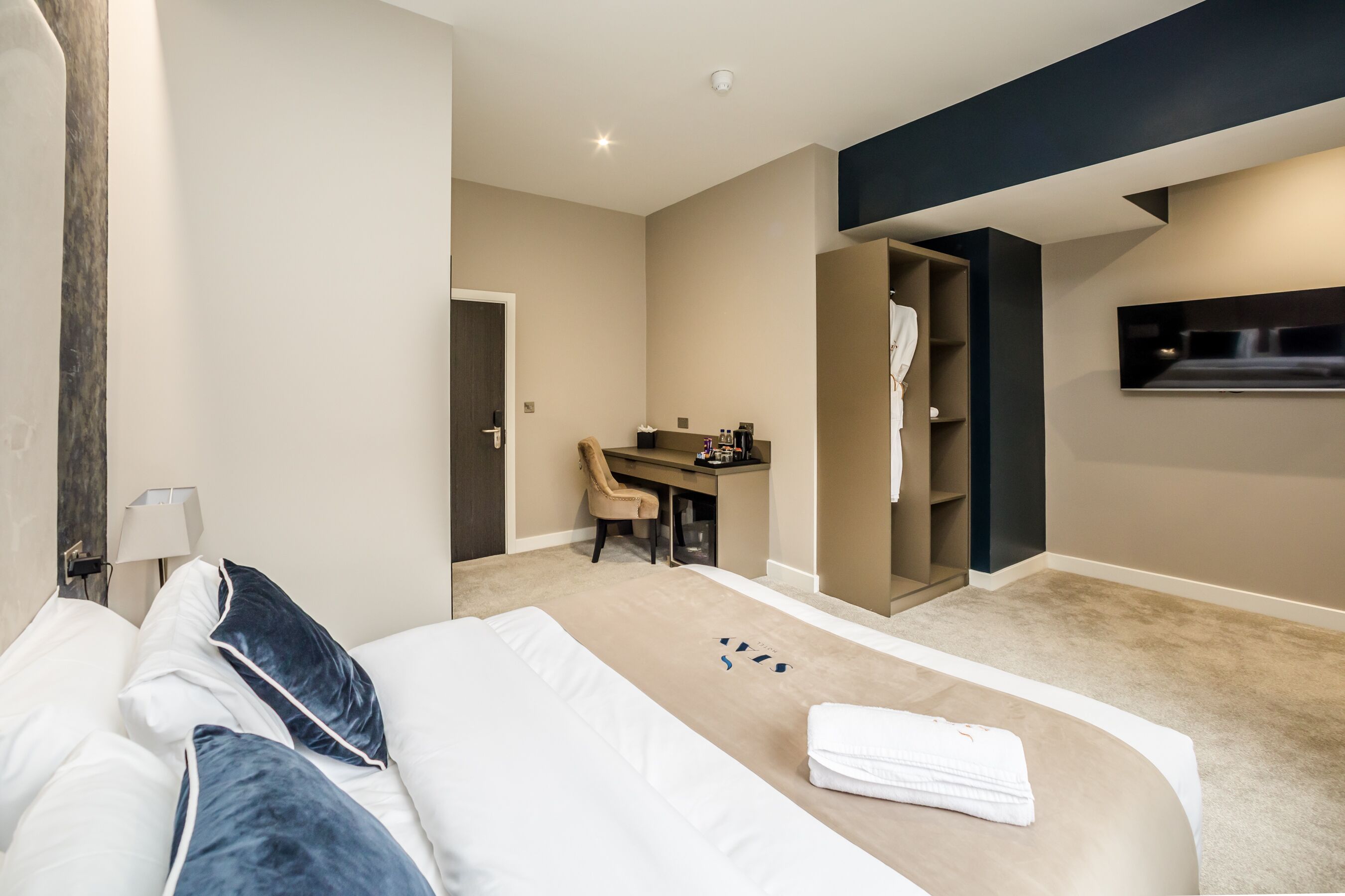 A modern hotel room with a large bed, a desk, and a walk-in closet.