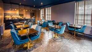 A modern restaurant with blue velvet chairs and gold accents, featuring a marble bar and large windows. - Stay Hotel (Huddersfield)