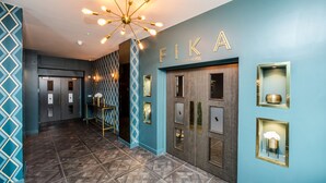 A hallway with a geometric patterned floor, a blue wall with the name 'FIKA' and a modern chandelier. - Stay Hotel (Huddersfield)