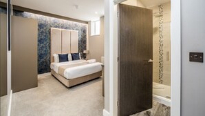A modern bedroom with a large bed, a walk-in closet, and a shower area. - Stay Hotel (Huddersfield)